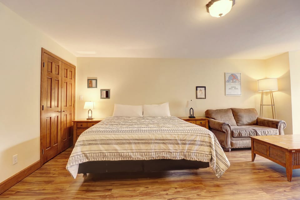 Spacious studio bedroom featuring a comfortable king bed, warm wood furnishings, and a cozy sofa for relaxing after a day of mountain activities.