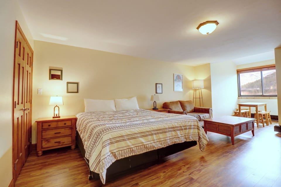 Bright and spacious studio-style bedroom with a king bed, warm wood furnishings, and a cozy sitting area—ideal for relaxing after a day on the slopes.