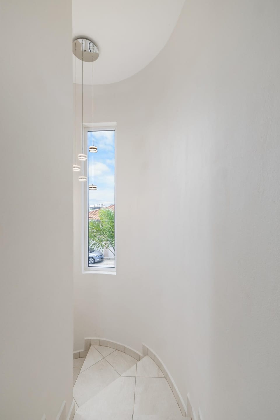 Elegant curved staircase with a tall window and modern pendant lighting.