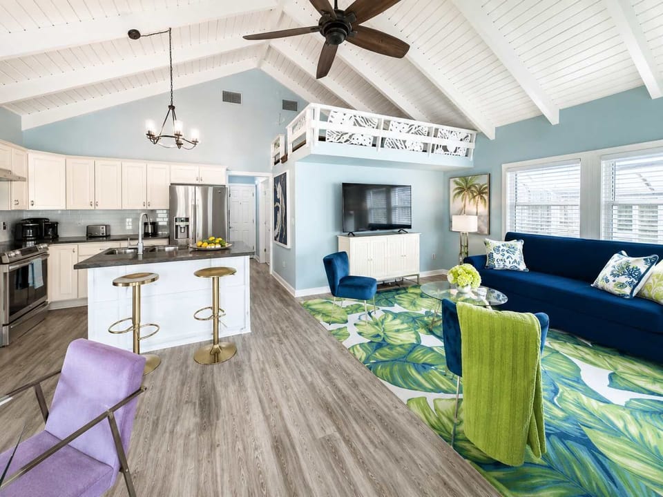 Bright and airy living room with plush seating, flat-screen TV, and floor-to-ceiling windows showcasing breathtaking Gulf views.