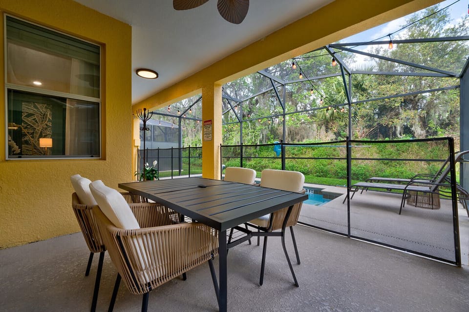 Screened-in covered patio with an outdoor dining table and view of the pool.