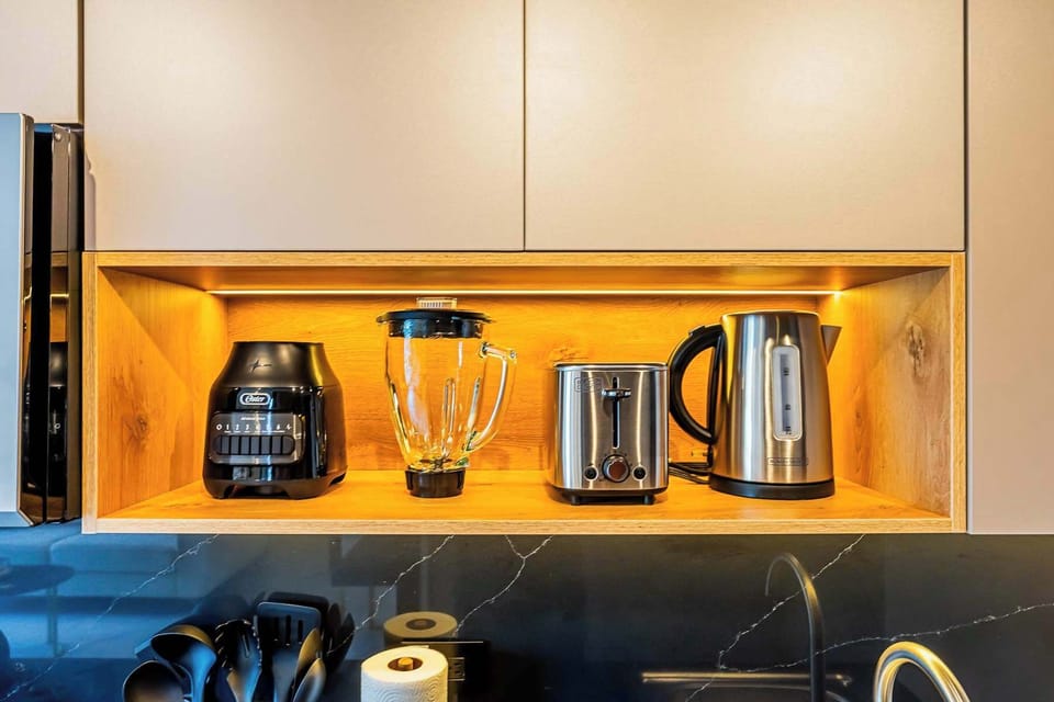 Kitchen shelf with toaster, kettle, blender, and cups with ambient lighting.