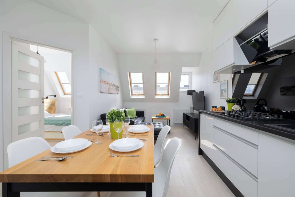 A modern open-plan kitchen with sleek black and white finishes, complemented by a spacious wooden dining table perfect for shared meals.