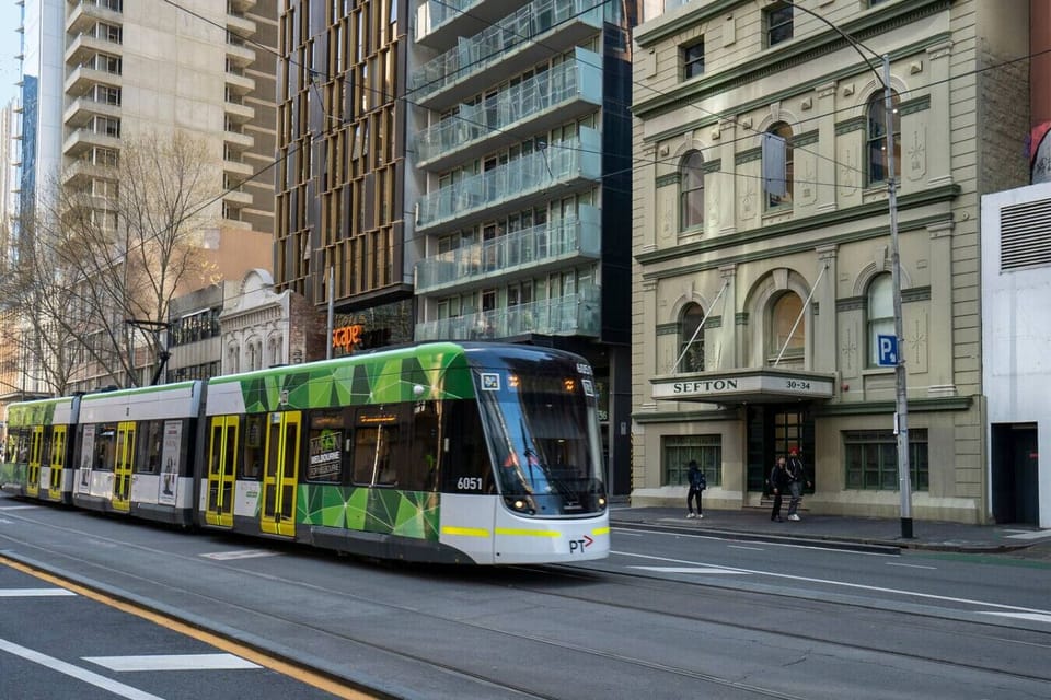 Modern city street view with a Melbourne tram passing historic and contemporary buildings. Enjoy direct access to public transport, dining, and shopping right outside the door.