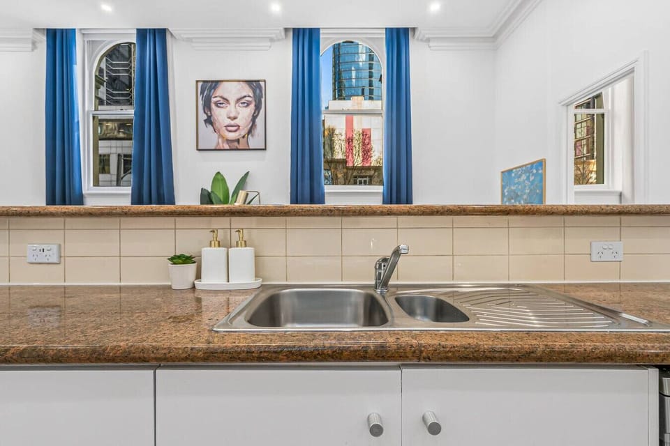 Bright kitchen sink area with granite countertops, double stainless basin, and modern fittings. Framed by large arched windows with city views, offering natural light and a clean, fresh space for daily use.