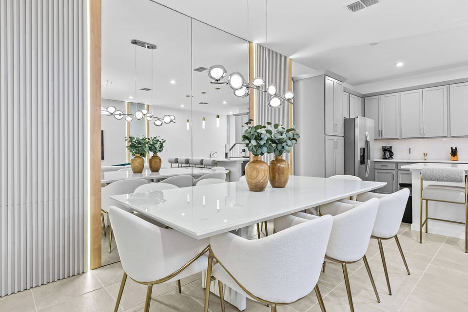 Enjoy your meals in this chic dining area with a sleek white table and modern chairs featuring gold accents. The bright space, adorned with mirrored walls and elegant pendant lighting, sets the perfect atmosphere for gatherings.