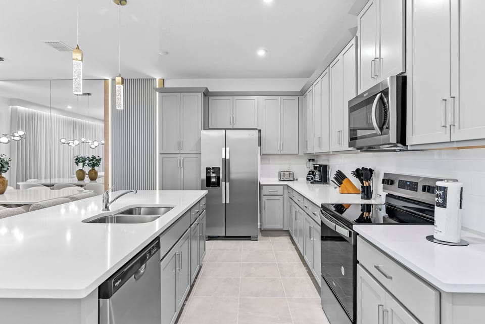 This stylish kitchen features soft gray cabinets and bright white countertops, creating an inviting atmosphere. With modern stainless steel appliances and charming pendant lighting, it’s perfect for all your culinary adventures.