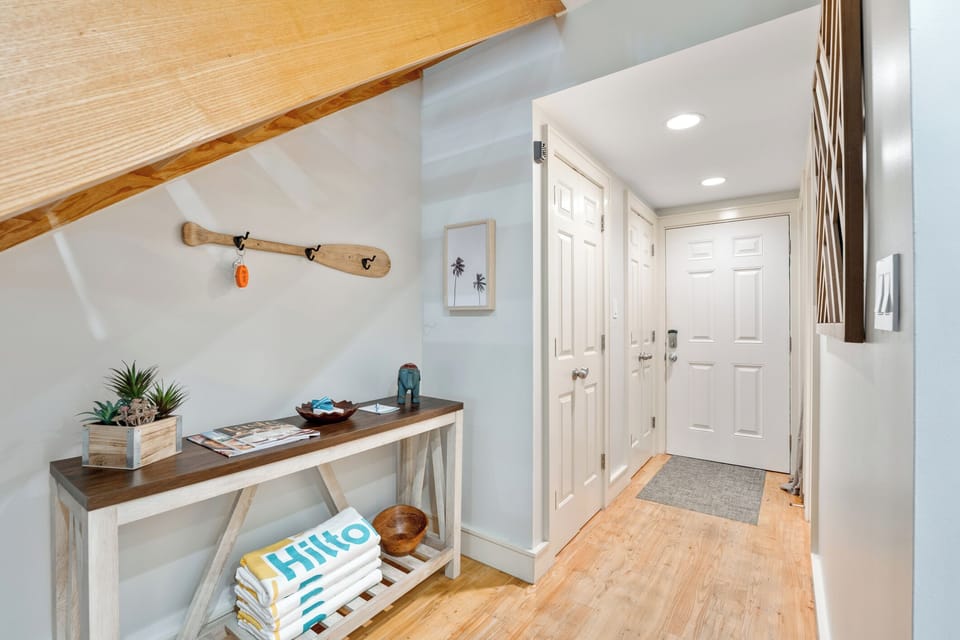 Coastal-themed entry console with a wooden oar key holder, stacked towels, and bright natural wood accents under a vaulted staircase.