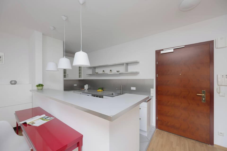 An open-plan kitchen with a small bar counter and overhead lights. The red stool adds a splash of color to the neutral design.