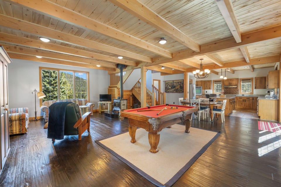 Open-concept living and dining area - with cozy couches centered around a soapstone woodstove, a smart tv, sound system, the billiard table, and a central dining table with comfortable seating for 4.