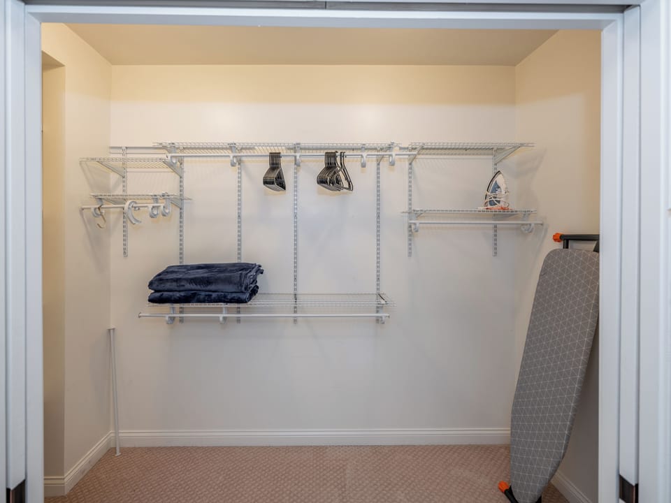 A large walk in closet with ample shelves, hangers, blankets and iron