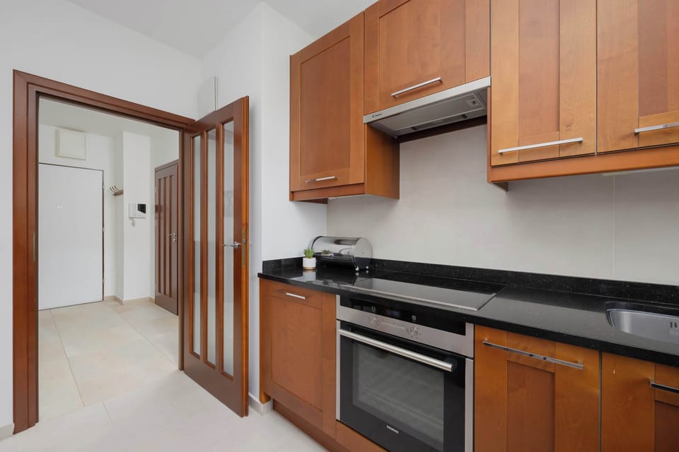 A kitchen with wooden cabinets, a black countertop, and a dining table nearby. Plants bring a fresh element to the space.