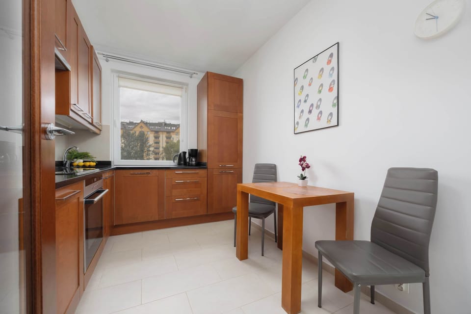 A kitchen with wooden cabinets, a black countertop, and a dining table nearby. Plants bring a fresh element to the space.