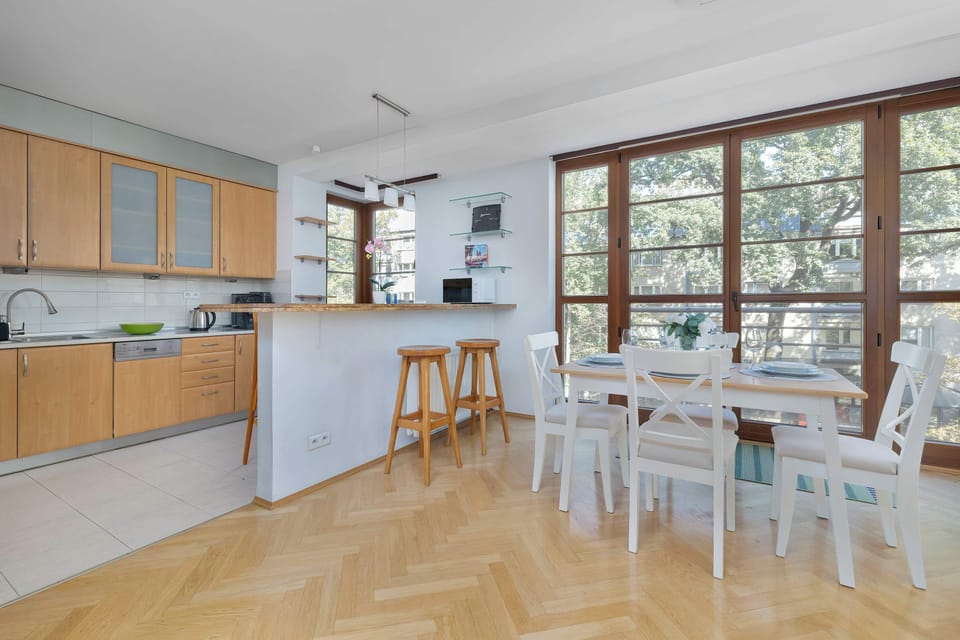 A kitchen with wooden cabinetry and a white countertop, featuring a dining bar and two stools. The space is functional and well-lit.