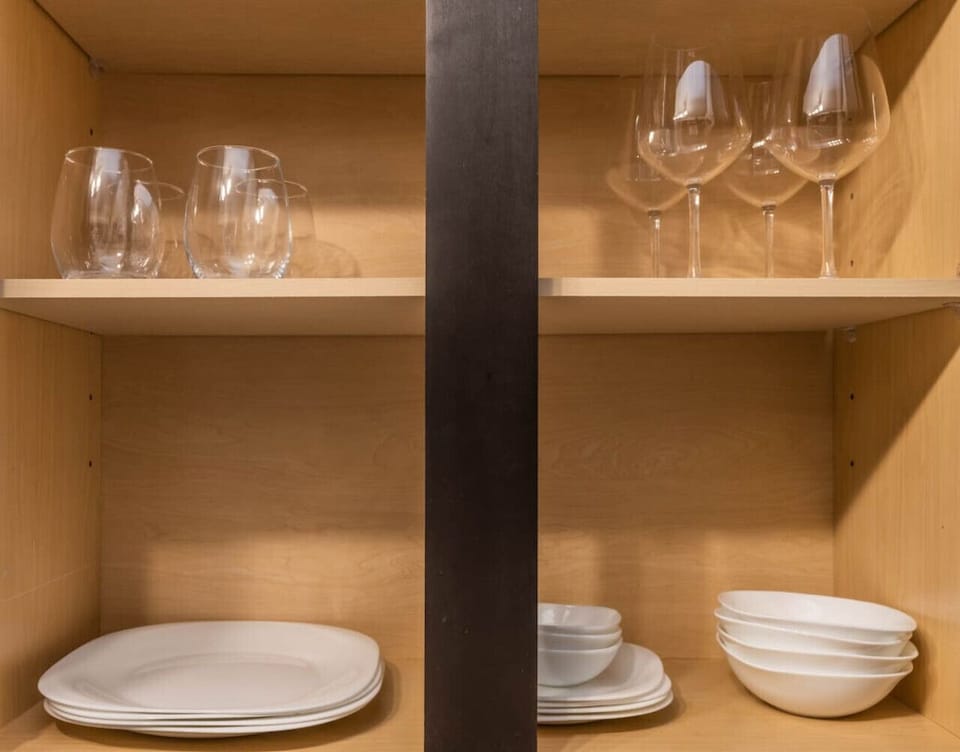 Fully Stocked Cabinet-Kitchen cabinet with mugs, plates, bowls, and glassware neatly arranged. Everything you need for dining and enjoying meals at home during your stay.