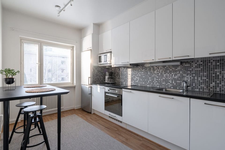 Fully equipped modern kitchen with sleek cabinets, oven, microwave, coffee maker, and a cozy breakfast table by the window.