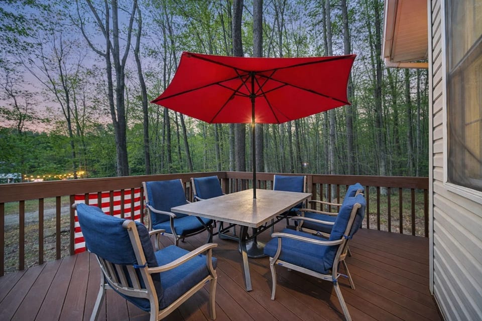 Outdoor Dining Retreat: Enjoy meals under a vibrant red umbrella amidst lush forest views!