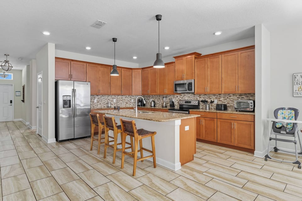 Welcome to a lovely kitchen with warm wooden cabinets and sleek stainless steel appliances, perfect for cooking. The spacious island and chic bar stools create an inviting space for casual gatherings and morning coffee chats.