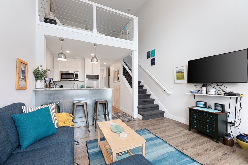 Open-concept living area w/ cozy sofa, loft above & seamless flow to the kitchen.