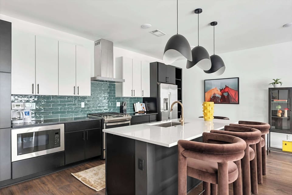 Dark cabinetry, white countertops, and that teal subway tile backsplash create a kitchen island where ten can gather to cook or grab coffee together. Reserve your stay with Misfit Homes