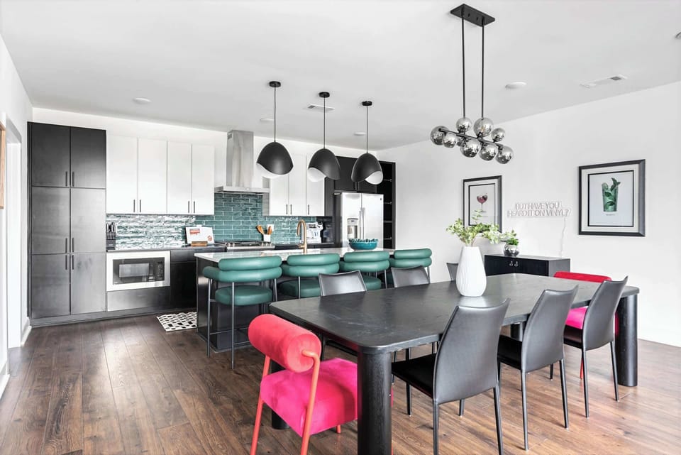 Kitchen island with green bar stools, a long dining table, and the teal backsplash create a gathering space designed for groups; everyone gets a seat and something to do