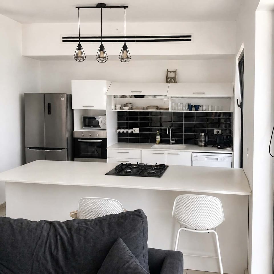 Modern open-concept kitchen featuring crisp white cabinetry, a black tiled backsplash, and an elegant island.