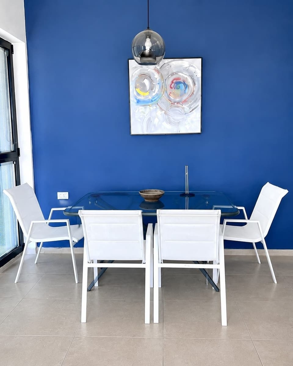 A vibrant blue feature wall highlights a glass dining table paired with minimalist white chairs.