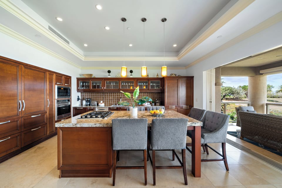 Cook and connect in this gourmet kitchen featuring a granite island, rich wood cabinetry, and seamless flow to a breezy outdoor lounge—perfect for tropical entertaining