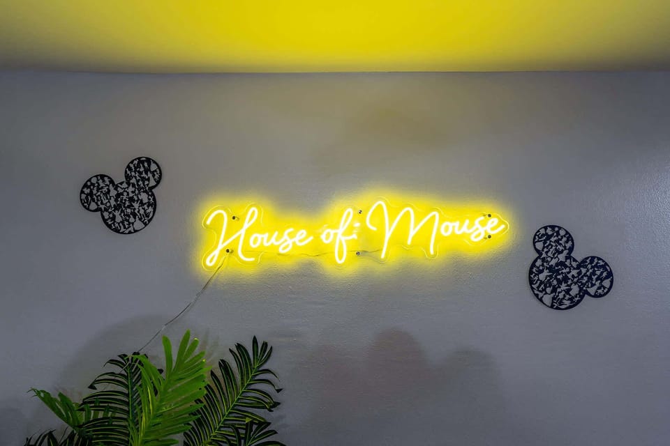 neon sign reading house of mouse with decorative wall art and plants