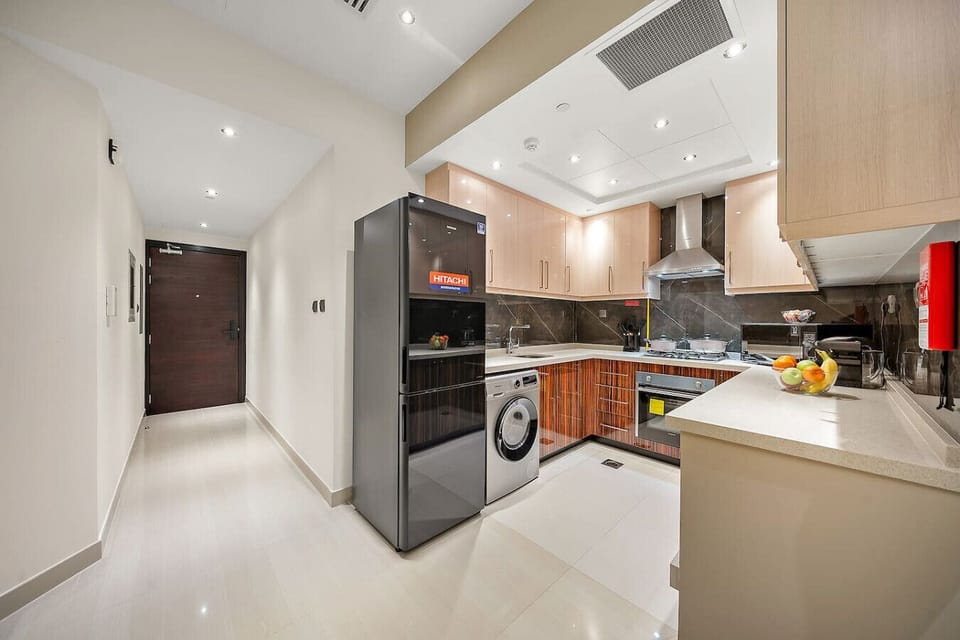 Modern kitchen with black fridge and light cabinets seen from entry hall.
