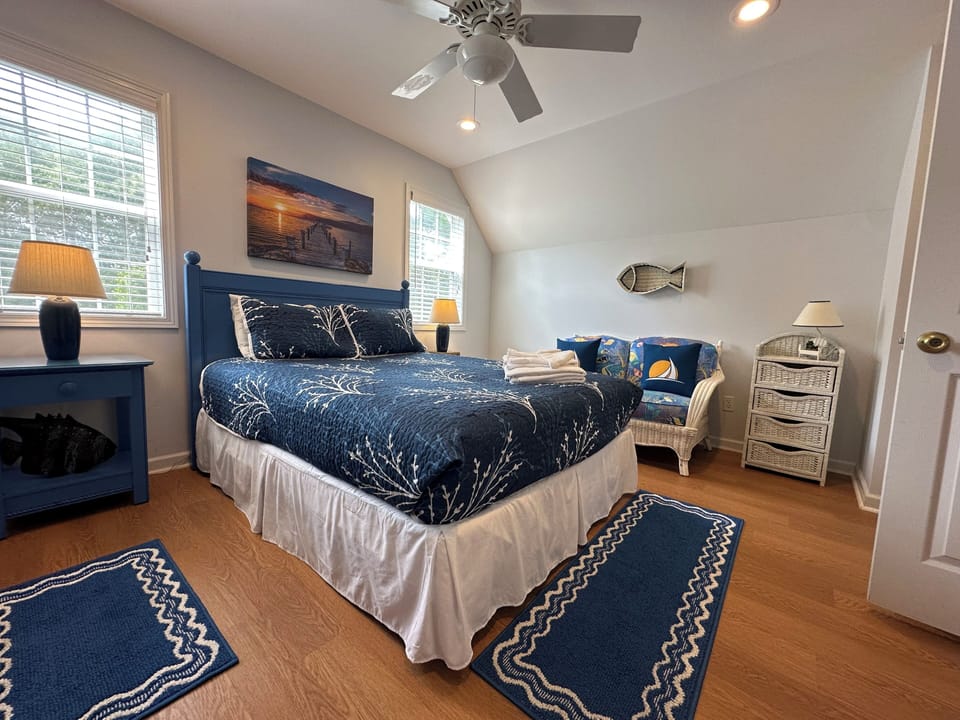 Drift off in your coastal-themed bedroom, where navy hues and nautical accents create a serene retreat. A ceiling fan keeps you cool while soft lighting sets a peaceful mood.