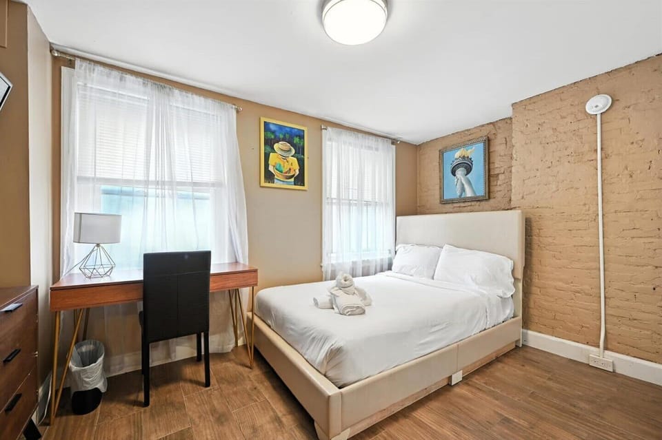 This bedroom offers a quiet retreat with a comfortable bed, a work desk for productivity, and a charming exposed brick wall.