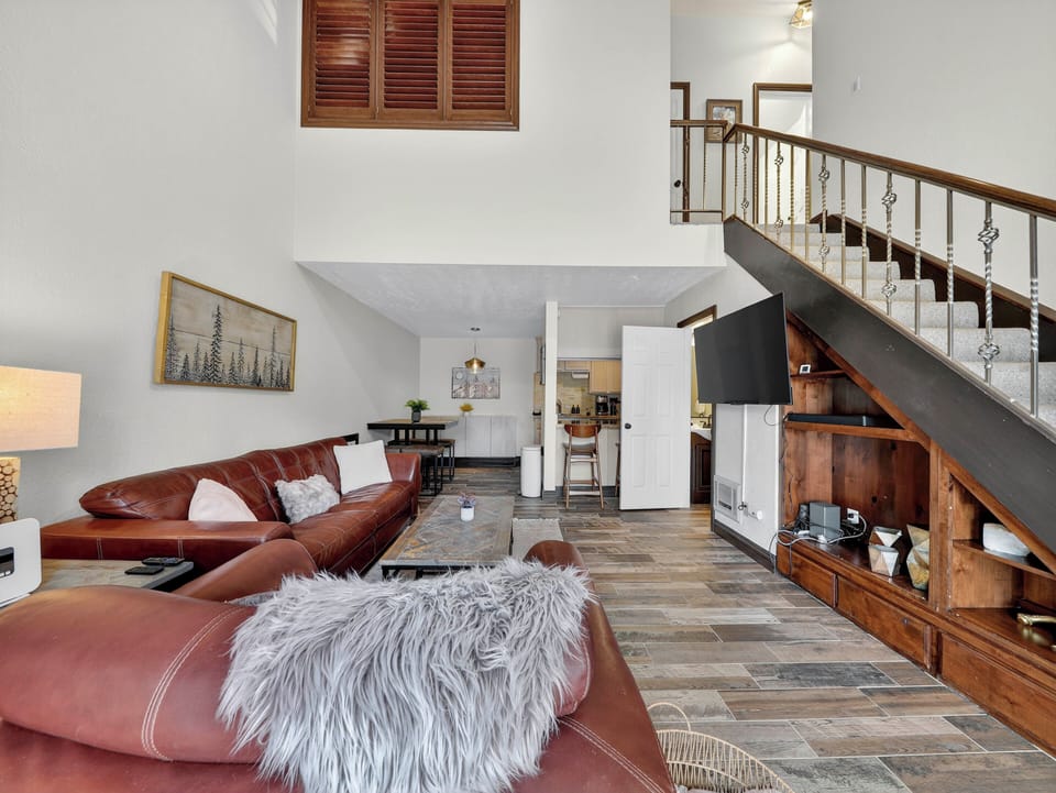 Bright and inviting living room with high ceilings, wood-burning fireplace, 55" flat-screen TV, and comfortable furnishings