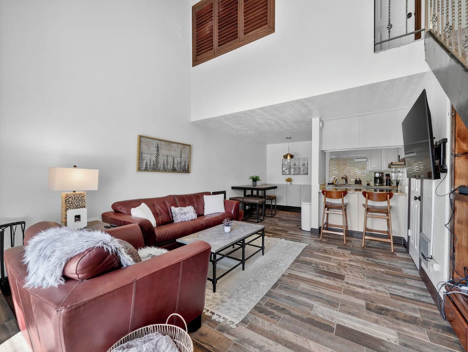 Bright and inviting living room with high ceilings, wood-burning fireplace, flat-screen TV, and comfortable furnishings