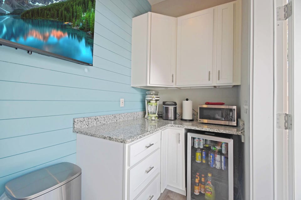 Outdoor kitchen has a refrigerator, microwave, ice maker and margaria machine.