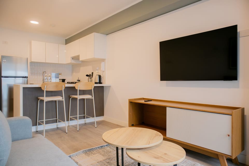 Open-plan kitchen and living room with bar stools, TV, and a bright modern aesthetic.