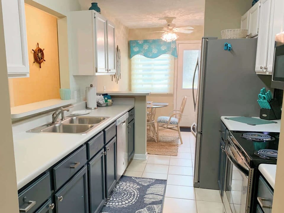 Bright and welcoming, this Hilton Head condo kitchen features fun blue cabinets paired with sleek stainless steel appliances. An additional dining area offers extra space for family meals, morning coffee, or game nights after a day at the beach.