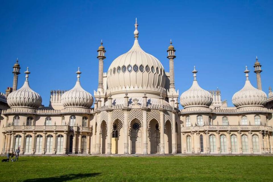 Majestic Royal Pavilion with its intricate domes and architectural splendor - Set against a bright blue sky, showcasing its regal and exotic design - Lush green lawn in front, inviting visitors to admire this historic landmark
