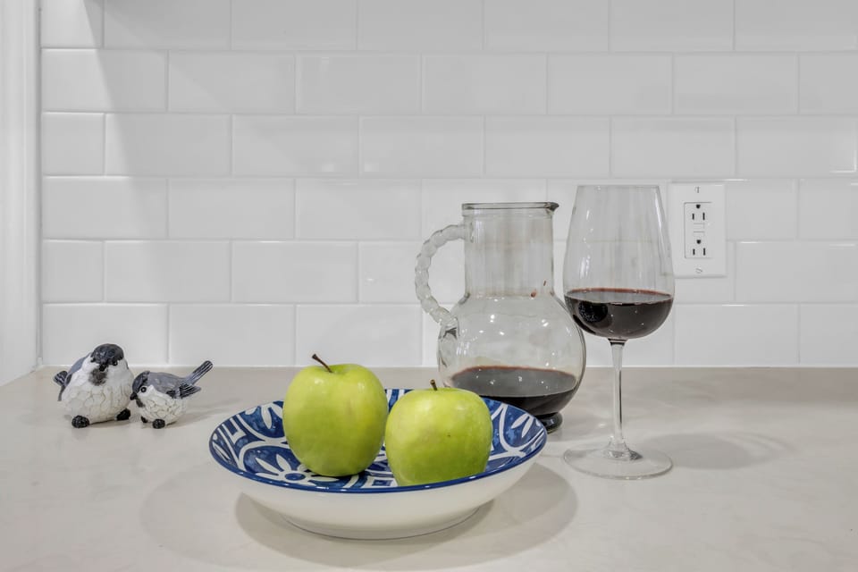 Green apples in blue bowl, wine pitcher/glass, bird figurines, white subway tile