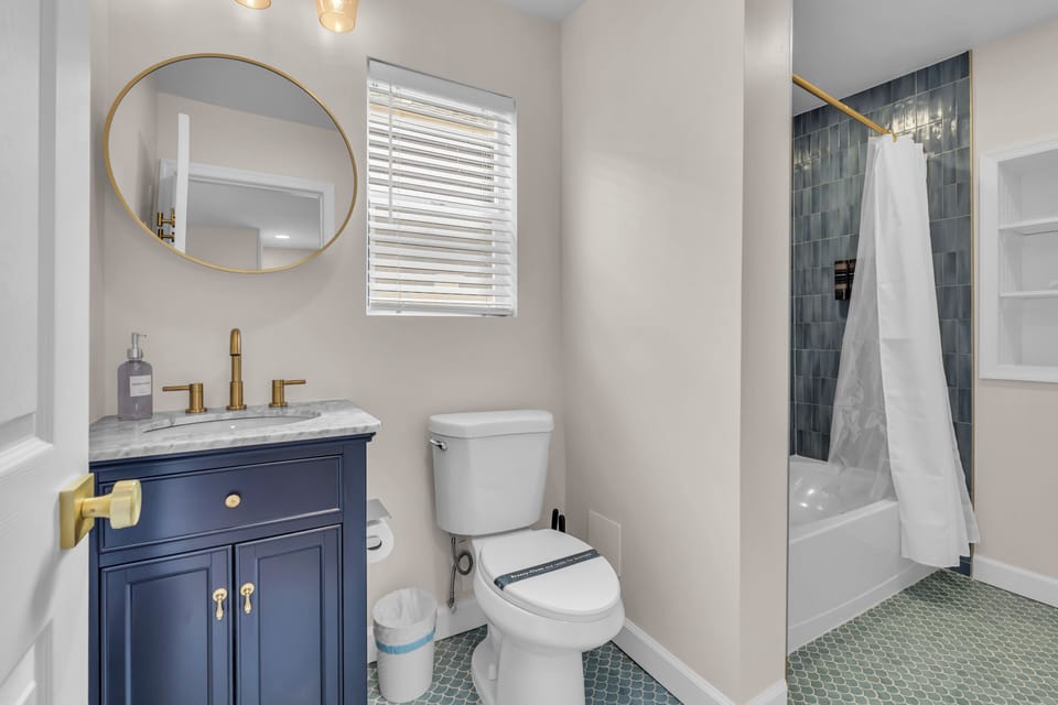 Full bath with navy vanity, gold fixtures, oval mirror, and modern lighting.