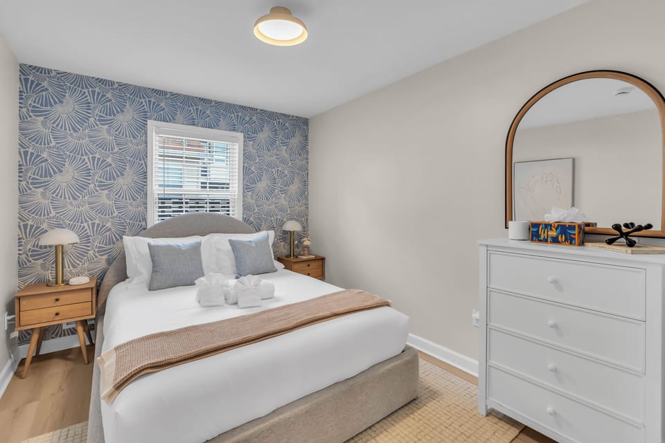 Bedroom with blue stripe wallpaper accent wall, queen bed with white linens, two nightstands, and table lamps.