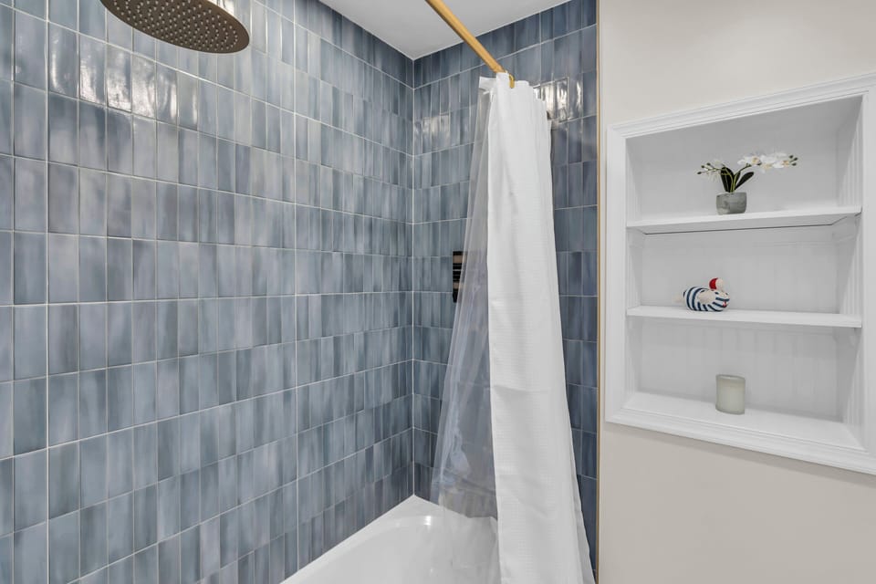 Full bath with walk-in shower, gray subway tile, white curtain, gold rainfall fixtures, and built-in shelving.