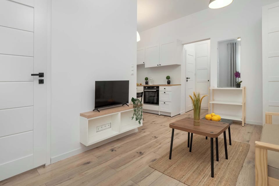 Another angle of the room showing the sofa, TV, and a desk on the side. Wooden flooring adds warmth to the modern look.
