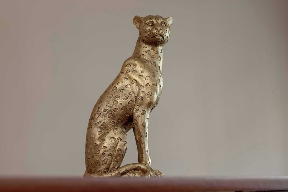 A small golden statue of a cat displayed on a shelf. It serves as a decorative accent in the home.
