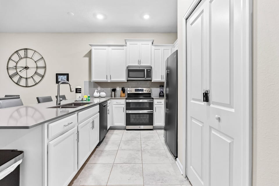 Step into a beautifully designed kitchen with stainless steel appliances and white cabinetry, complemented by light tile flooring. A charming clock adds character to this functional space, ideal for meal prep and gatherings.