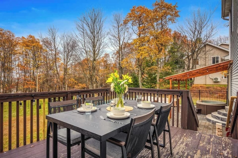 Outdoor dining area on the deck with fall foliage views and a hot tub nearby.