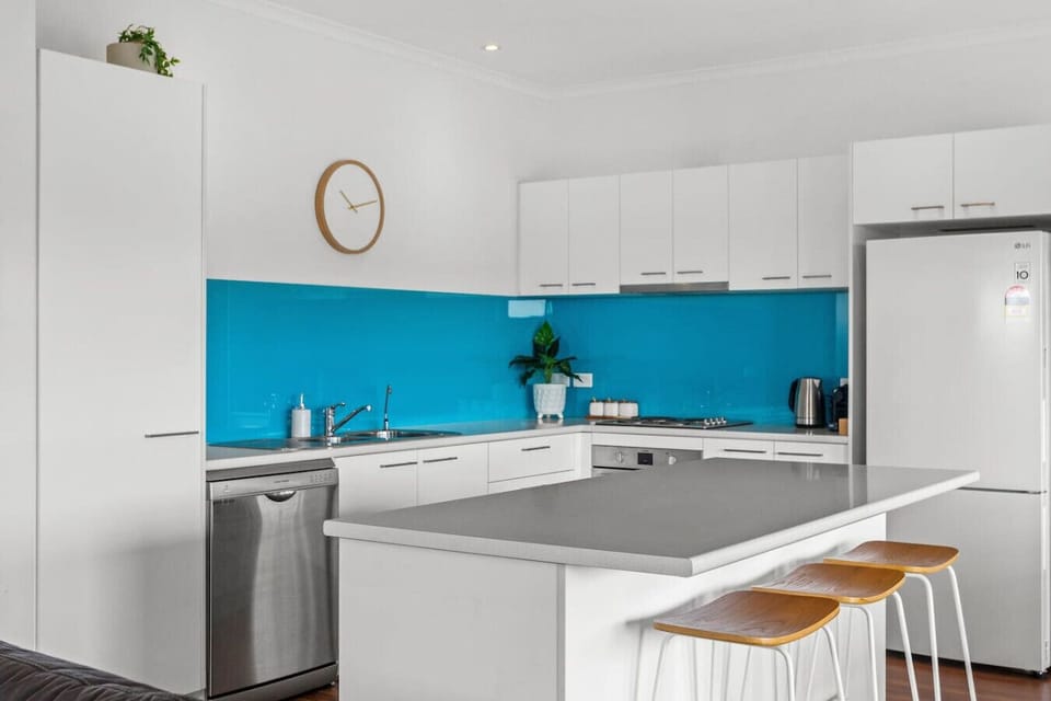 Cook with ease in the vibrant kitchen equipped with stainless steel appliances, a turquoise splashback, a Nespresso coffee machine, and island seating that invites conversation.
