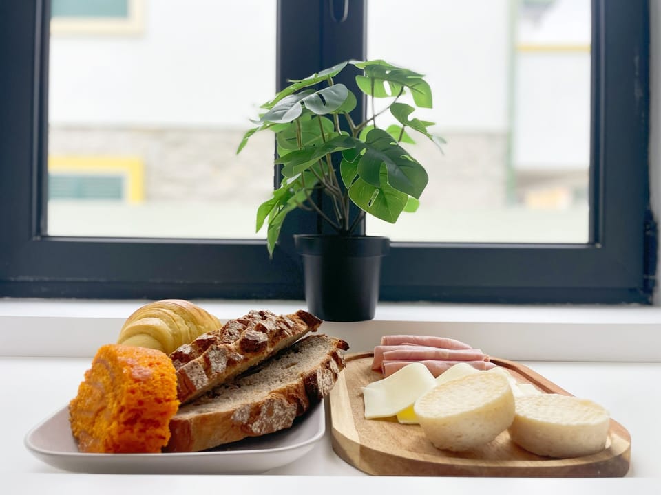 [Zona de Refeição]
Detalhe do pequeno-almoço com produtos locais: pão artesanal, bolos regionais, fruta fresca e bebidas. Uma mesa preparada com carinho para começar bem o dia.
