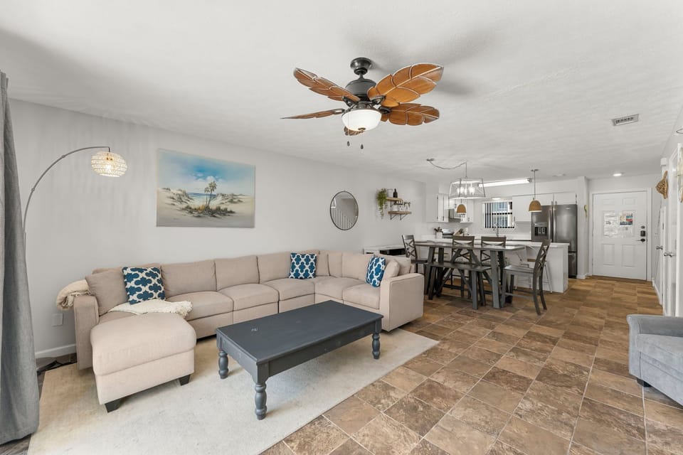 Spacious living area with a large sectional sofa and tropical ceiling fan adjacent to the dining space.
