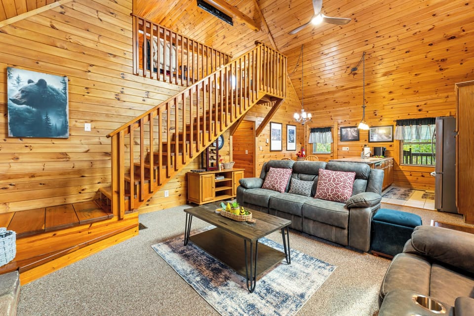 Relax in the spacious living room featuring plush sofas, a stone fireplace, smart TV, and cozy cabin décor